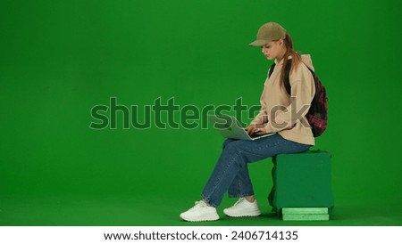 Portrait of person tourist isolated on chroma key green screen background. Young woman sitting working on laptop, waiting for flight.