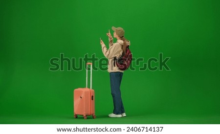 Portrait of person tourist isolated on chroma key green screen background. Young woman with suitcase holding smartphone and looking at the departure board.