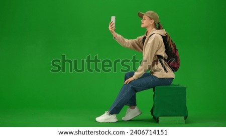 Portrait of person tourist isolated on chroma key green screen background. Young woman sitting holding smartphone and taking selfie pictures.