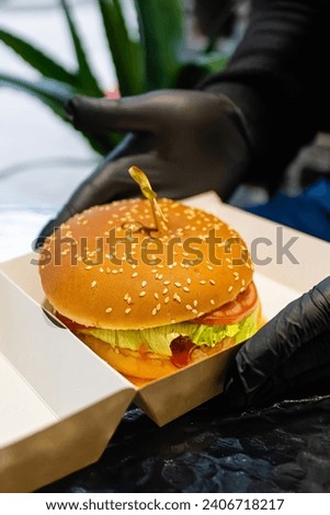 Holding a hamburger in his hands. Delicious appetizing burger.Fast food cafe.American food.Burger recipe.Cafe menu.Appetizing 
feed.Home delivery of food.food in a box.juicy burger.client.
eating.