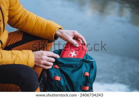 A guy puts a first aid kit in a backpack, packing things for a hike, safety in a winter trip, trekking in the mountains. personal first aid kit. High quality photo Royalty-Free Stock Photo #2406734243