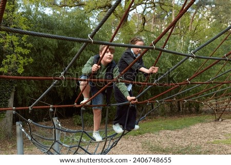A teenage boy and girl climb onto a spider's web ride on a walk in the park.