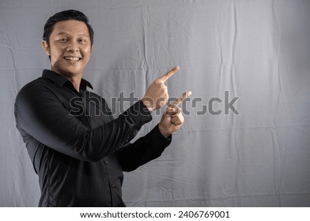 Asian businessman wearing a black shirt is smiling with a gesture pointing at something