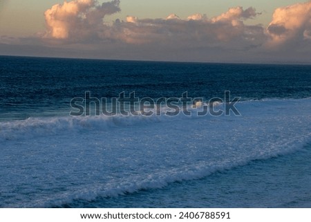 Sunset skies above an ocean with big waves. crashing on shore