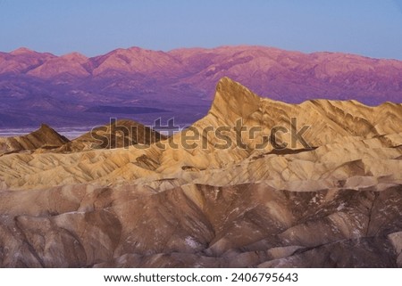 Golden hour sunrise over layered mountain rock formations at Zabriskie Point Death Valley National Park California Royalty-Free Stock Photo #2406795643