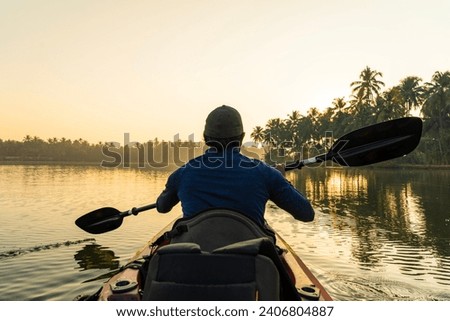 Young man kayaking in Kavvayi Island Kannur, Kerala travel and tourism concept photo, Rear view of man canoeing in a lake Royalty-Free Stock Photo #2406804887