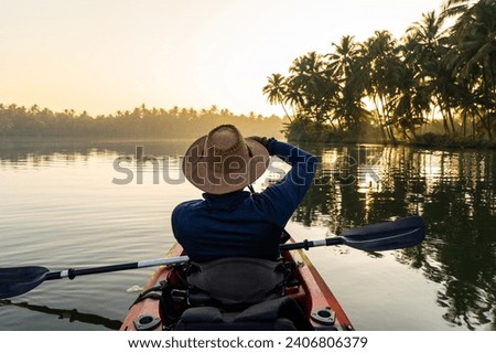 Tourist taking photos on kayak in Kavvayi Island Kannur, Kerala travel and Tourism concept photo, Travel photography background, beautiful sunrise view of lake with palm trees on the background Royalty-Free Stock Photo #2406806379