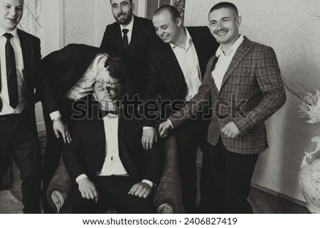 A young groom and his funny friends pose for the camera. A group of young people hug the groom and cheerfully congratulate him. Happy friends. Friends in the room. Wedding day. Black and white photo.