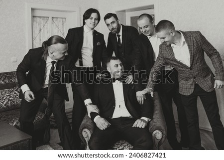 A young groom and his funny friends pose for the camera. A group of young people hug the groom and cheerfully congratulate him. Happy friends. Friends in the room. Wedding day. Black and white photo.