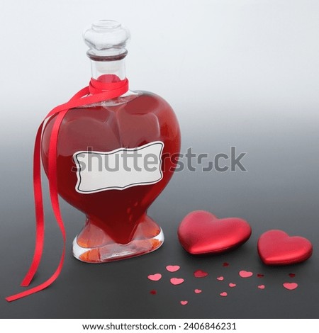 Love potion magical concoction or perfume gift in heart shaped bottle with red heart decorations on gradient gray. Valentines Day lovers abstract concept. Royalty-Free Stock Photo #2406846231