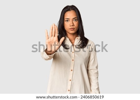 Young Filipina with long black hair in studio standing with outstretched hand showing stop sign, preventing you.