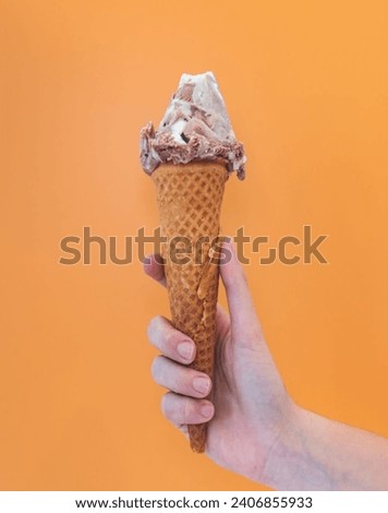 Chocolate ice cream scoop in waffle cone on orange background