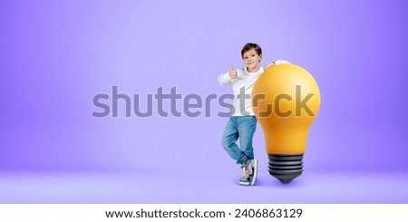 Child showing thumb up, full length standing near large light bulb on empty purple background. Concept of education, learning, art, creativity and idea
