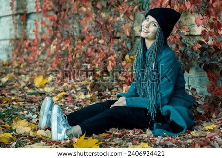 Portrait of a young beautiful girl with a smile on her face in an autumn park against a background of colorful leaves. A girl with dreadlocks and pigtails poses against the background of trees.