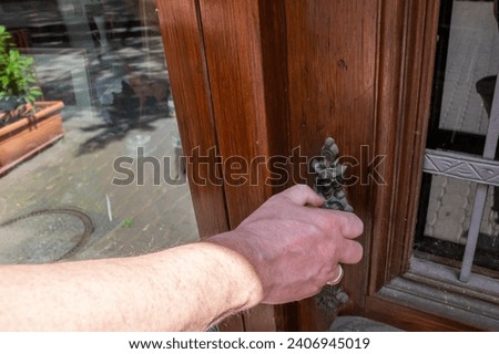 Man holding old metal door handle on the wood door. Vintage iron pen in old house. 