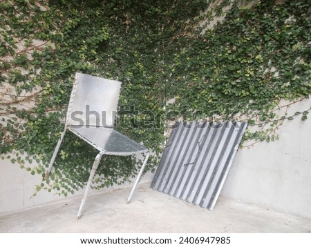 photo of a broken bench made of silver iron with a wall covered in green wild plants as a background