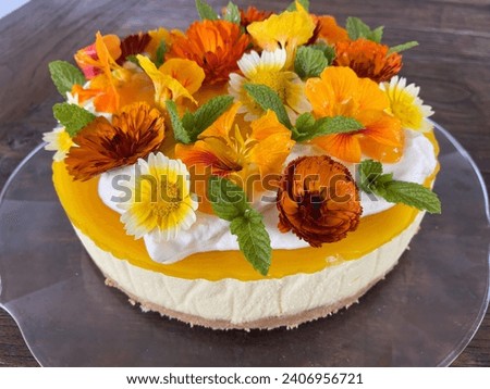 Rustic round sweet cake decorated with orange and yellow flowers, whipped cream and green mint leaves on a glass platter