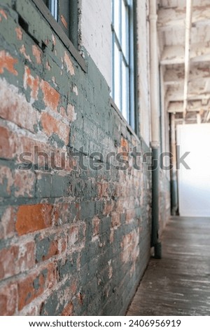 Industrial hallway flooded with natural light and high ceilings. Peeling paint on bricks and the worn, wooden flooring add to the character of the architecture. 