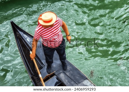 Venetian gondolier punting gondola through green canal waters of Venice Italy. Royalty-Free Stock Photo #2406959293