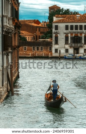 Venetian gondolier punting gondola through green canal waters of Venice Italy. Royalty-Free Stock Photo #2406959301