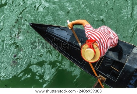 Venetian gondolier punting gondola through green canal waters of Venice Italy. Royalty-Free Stock Photo #2406959303