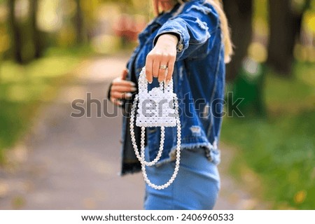 A stylish handbag in the hands of a young woman. Background with selective focus and copy space for text