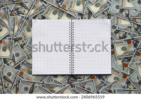 Office workplace table with blank notebook or notepad and many hundred dollar bills close up