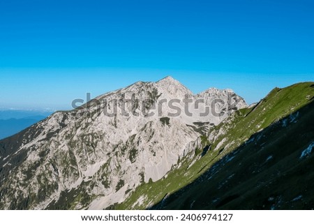 Scenic view of majestic mountain peak Hochstuhl (Stol) in untamed Karawanks, border Slovenia Austria. Looking through lush forest. Hiking wanderlust in wilderness of Slovenian Alps in summer Royalty-Free Stock Photo #2406974127