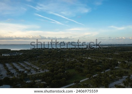 Wide landscape aerial drone view of the tropical beach surrounded by palm trees on Crandon Park in Key Biscayne with the skyline of Miami, Florida in the distance on a sunny summer evening