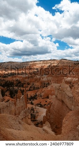 Wide landscape vertical nature view of a large valley of orange sandstone hoodoo formations surrounded by greenery and trees in the desert of Southern Utah on a warm sunny summer day