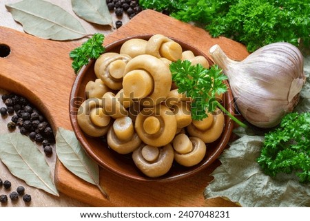 Marinated champignon mushrooms. Mushrooms with herbs and spices. Canned champignons on a plate. Mushrooms with parsley, garlic, bay leaf and peppercorns. Royalty-Free Stock Photo #2407048231