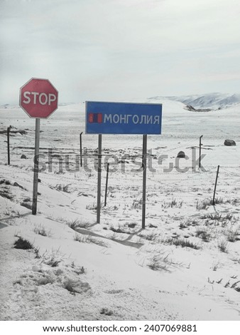 Sign marking the border crossing with Mongolia. Border is on a snowy mountain slope. Fence with barbed wire on the background winter snow slope.