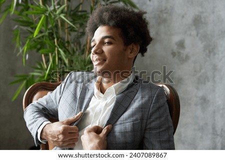Side view of arrogant narcissistic self-centered african american businessman sitting in leather armchair adjusting his gray stylish elegant jacket, feeling proud of his business project and success Royalty-Free Stock Photo #2407089867