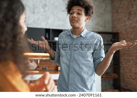 Young black afro guy explaining something to his african american girlfriend standing with back turned to camera, gesticulating and shrugging his shoulders trying to make excuses of his behavior Royalty-Free Stock Photo #2407091161