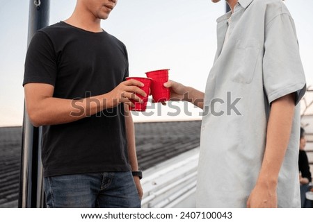 Two interesting young Asian male friends are toasting beers and enjoying talking while partying on a rooftop bar together. Friendship and night life concepts. close-up image