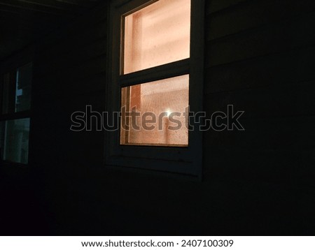 The view of a single candle in a window at night time from outdoors.