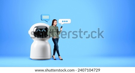 Smiling woman looking at phone in hand, standing full length near cartoon AI robot with speech bubbles on copy space empty blue background. Concept of virtual assistant and bot communication