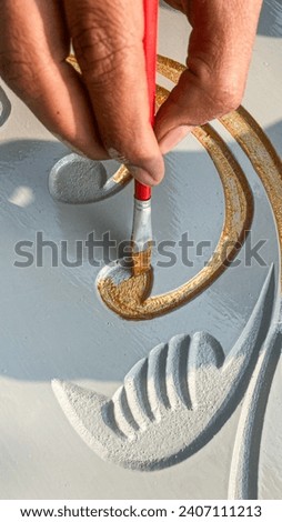 Artists Hand making beautiful designs with red painting brush with golden colour