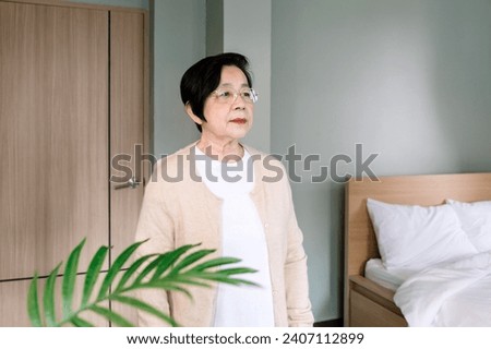 Senior Asian woman waiting assistance or helping hand of Asian woman nurse in the bedroom, home caregiver will visit at the entrance. Home health care and nursing home concept