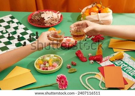 The two of them were clinking two beer glasses, a seahorse and chess set was displayed on the table with a variety of jams, dried nuts, a basket of tangerines and lucky money envelopes. Copy space.