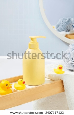 Close-up of a light yellow shower gel bottle displayed on a wooden tray with silicone ducks. Simulate bathroom space with body care products. Blank labels for design and branding.