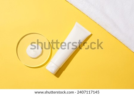 A drop of white cosmetics on a glass podium and an unlabeled cosmetic tube displayed on a yellow background. Build a cosmetic brand with mockups. Royalty-Free Stock Photo #2407117145