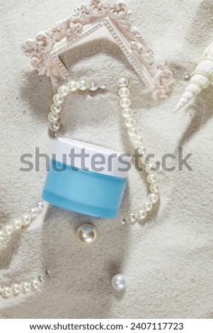 On the smooth sand, an unbranded cosmetic jar, pearl necklaces and ornaments are displayed. Cosmetics advertising with sophisticated space. Summer mood.
