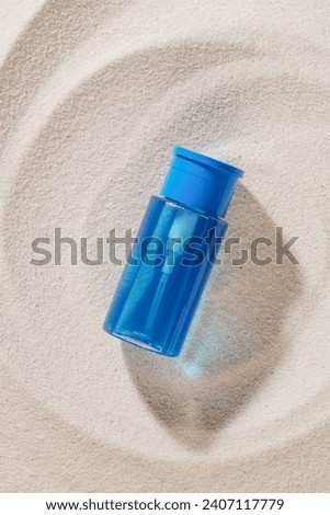 A transparent blue bottle of makeup remover stands out against the smooth sand background. Natural beauty. Exquisite copy space for cosmetics advertising. Skin care product concept.