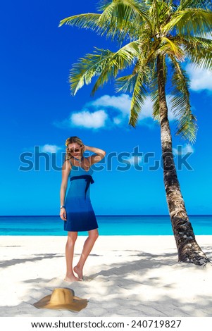 beautiful young woman with long blond hair  relaxes under the palm three. The blue sea in the background