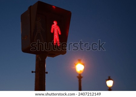 Red pedestrian traffic signal at dusk with street lamps in the background
