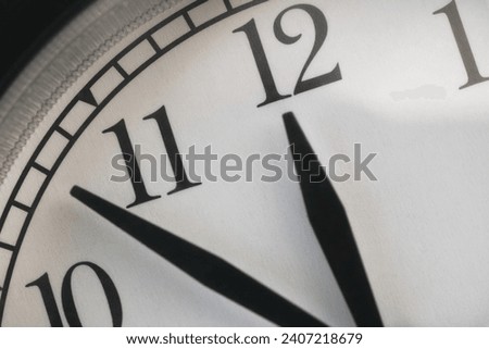 A clock with the hour hand pointing at twelve and the minute hand between 10 and 11. Close up.