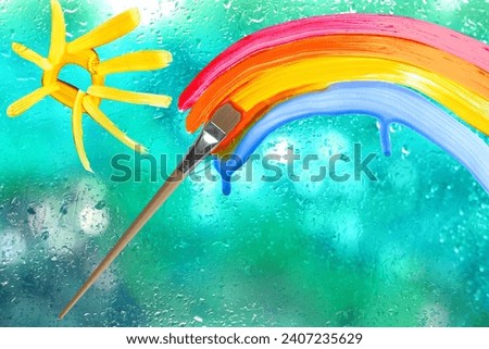 painting rainbow, sun on glass, brush, rain outside window, creative development, happy childhood, texture blue glass background with water drops, place for text, horizontal banner with blurry bokeh