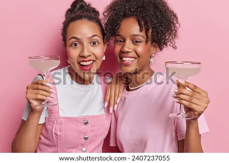 Image of positive cheerful woman with long nails wear jewellery have fun together on party hold glass of cocktail smile happily enjoys spending time together isolated over pink studio background.