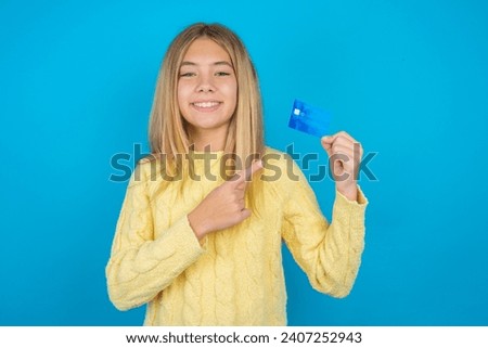 Photo portrait of Beautiful kid girl wearing yellow sweater doing purchase with pointing finger credit bank card